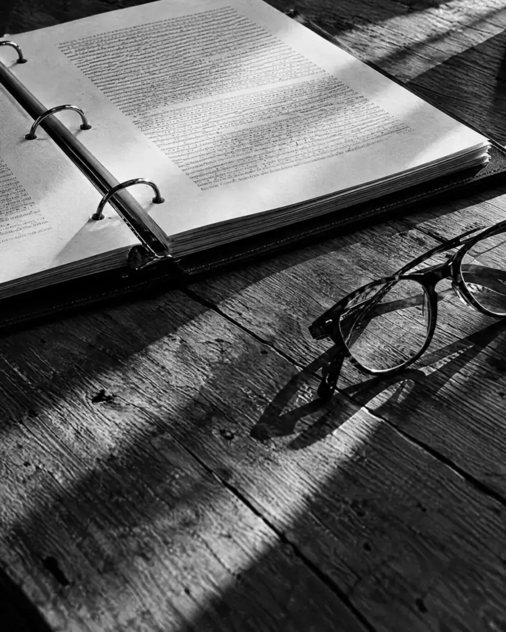 Aufgeschlagener Ordner mit bedruckten Seiten und Lesebrille auf einem Holztisch