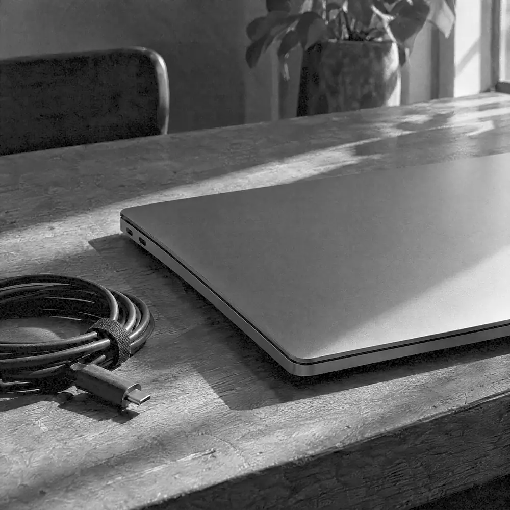 Geschlossener Laptop schräg auf einem Holztisch, daneben ein aufgerolltes Kabel