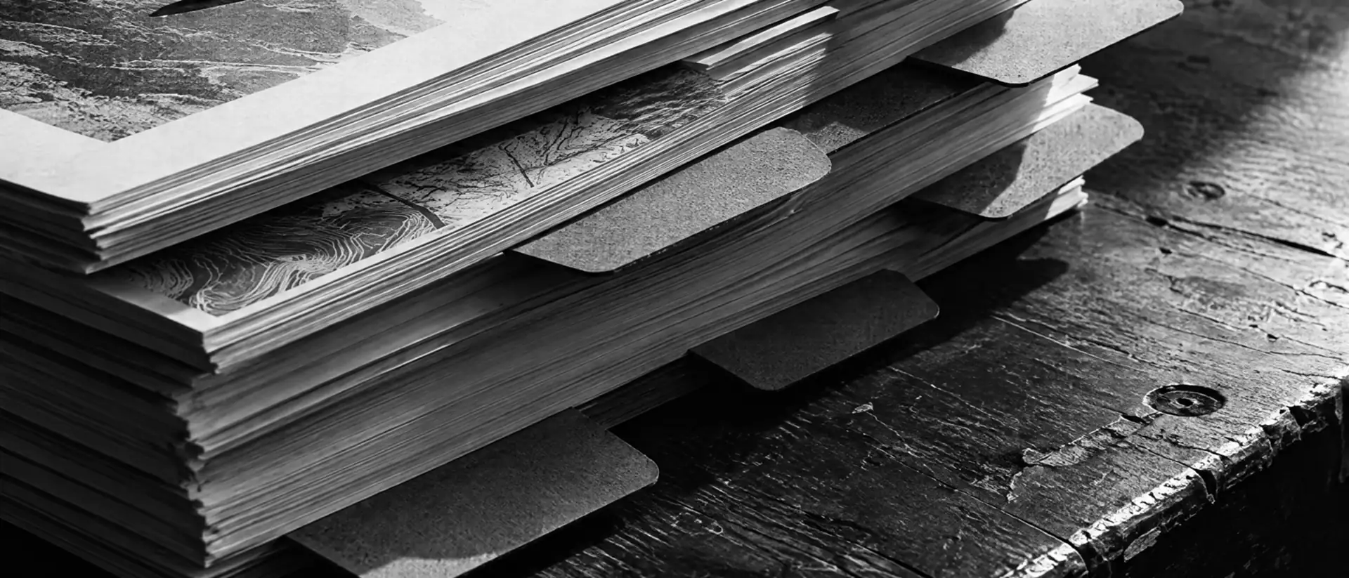 Stapel ausgedruckter Unterlagen mit herausragenden Registerreitern und Stift auf einem Holztisch im harten Seitenlicht